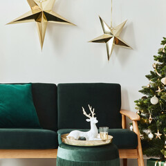 Stylish christmas living room interior with green sofa, white chimney, christmas tree and wreath, stars, gifts and decoration. Family time. Template.