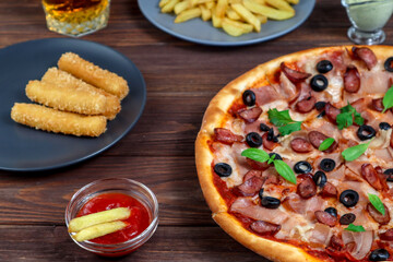 Pizza on a platter close-up on the table with ketchup, juice, sauce and potatoes on a dark wooden table in the rustic style.