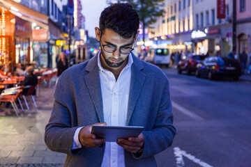 Germany, Munich, young businessman using digital tablet in the city at dusk