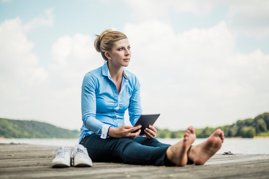 Woman sitting on jetty at a lake using tablet