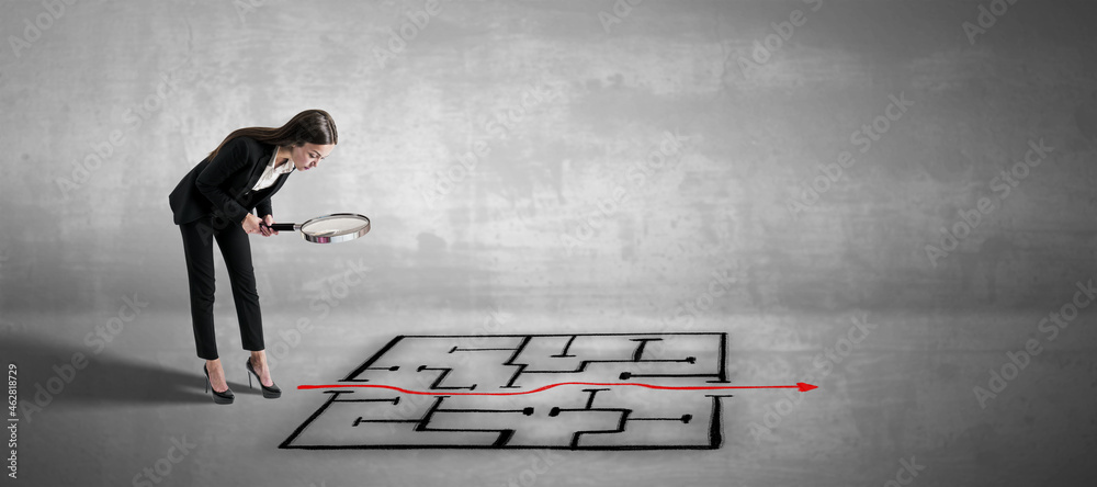 Poster attractive young businesswoman with magnifier looking at maze and arrow sketch on concrete backgroun