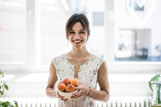 Woman holding bol of apricots in her kitchen