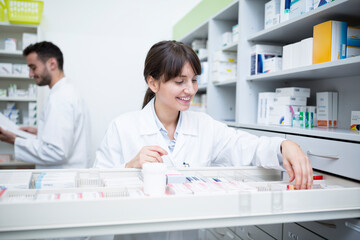 Smiling pharmacist seeking out medicine at cabinet in pharmacy