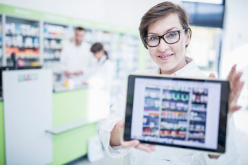 Portrait of smiling pharmacist in pharmacy showing tablet