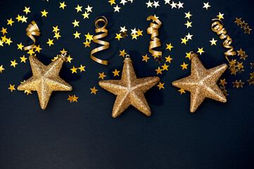 Fototapeta na wymiar Christmas frame made of shiny golden stars, streamers, decorations on a black background