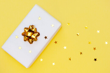 Gift box on a yellow background with gold confetti. 