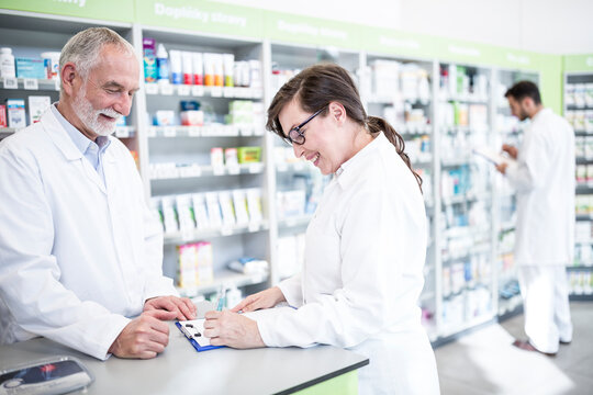 Two smiling pharmacists with clipboard at counter in pharmacy