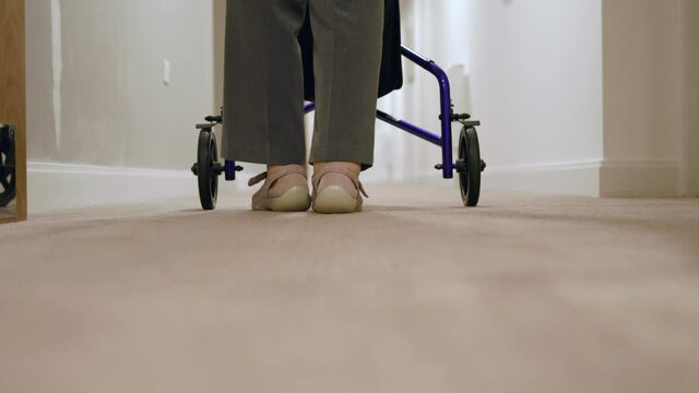 Close Up Rear View Of Senior Woman With Walker Walking Along Corridor In Retirement Home