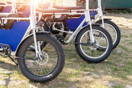 Many retro fat electric bicycle scooters parked on dirt grass field outdoor ready for hire rental sharing cpuntry parl leisure recreation trip. E power transport rent equipment. Rural offroad cycling