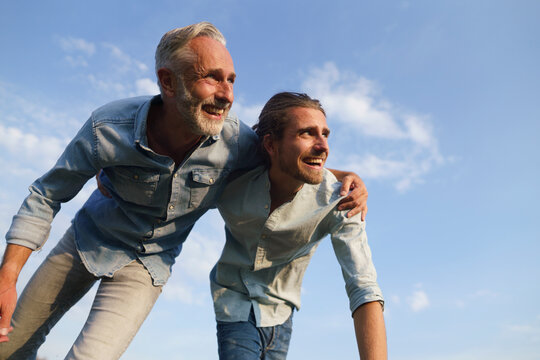 Carefree father with adult son under blue sky - Powered by Adobe