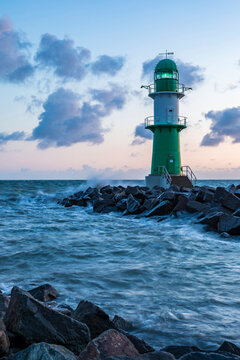 Germany, Mecklenburg-West Pomerania, Warnemunde, Lighthouse and sea waves crashing against rocks at dusk