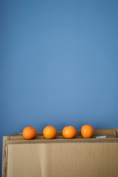 Four oranges on cardboard against blue wall