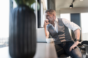 Serious mature businessman with laptop looking out of window
