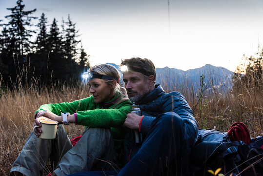 Hiking couple taking a break in the evening, wearing head lamps, drinking tea