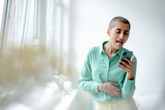Woman in a loft using smartphone sticking out her tongue