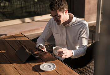 Young man using cell phone and tablet at outdoor cafe