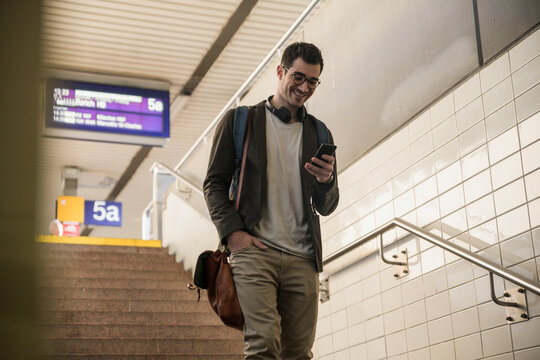 Smiling young man with cell phone walking down stairs at the station