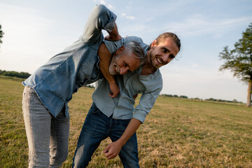 Happy father and adult son playfighting on a meadow in the countryside