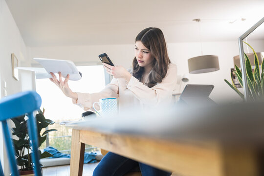 Young woman sitting at table at home holding smartphone and plane model