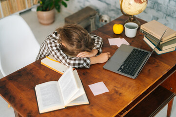 High-angle view of tired little child school girl sleeping at work desk lying on notebooks, exhausted child schoolgirl feeling lazy and unmotivated, doing boring school homework assignments.