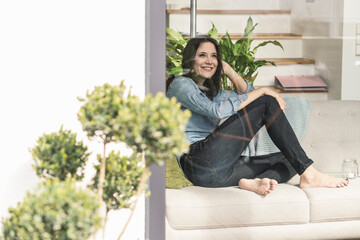 Happy woman sitting on couch behind windowpane at home