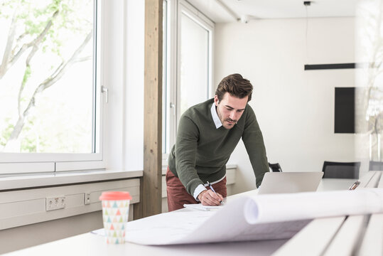 Young architect working on blueprint in bright office