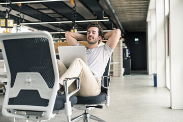 Young businessman working relaxed in modern office, with laptop on lap