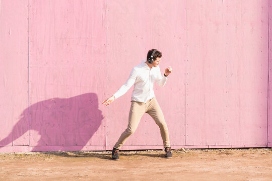 Exuberant young man listening to music in front of pink wall