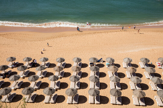 High angle view of lounge chairs and parasols at sandy beach during summer, Albufeira, Algarve, Portugal