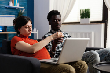 Pregnant interracial couple relaxing and using technology. Mixed race people expecting child,...