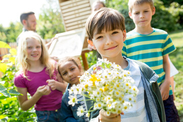 School children learning about herbs in nature studies, boy holding bunch of chamomile