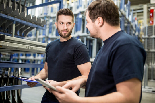 Two workers with clipboard and tablet in factory warehouse