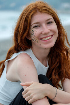 Smiling woman with small stones and sand on face sitting on beach