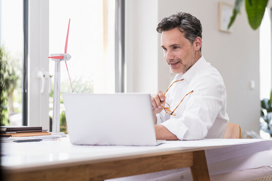 Businessma n sitting in office, using laptop, looking at model of a windwheel