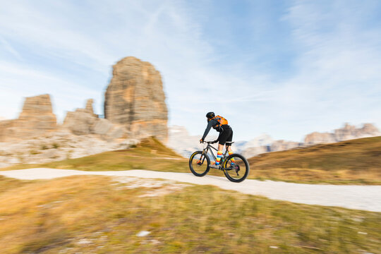 Italy, Cortina d'Ampezzo, panning view of man cycling with mountain bike in the Dolomites mountains