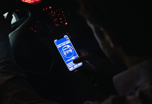 Close-up of young man adjusting brightness of cell phone in car at night