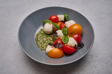 Delicious italian caprese salad with ripe tomatoes, pine nuts, basil and mozzarella cheese in grey deep plate. Close up 