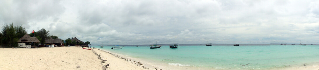 Fototapeta na wymiar Panorama Photo Of A Cloudy Day At The Beach Of Nungwi In Zanzibar With Locals Boats On The Clear Ocean Water