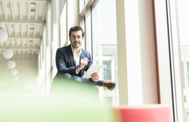 Young businessman sitting in lounge, using digital tablet