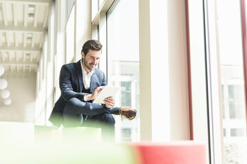 Young businessman sitting in lounge, using digital tablet