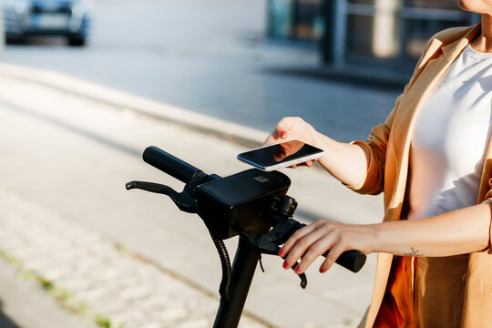Mature female professional using mobile phone for scanning QR code on electric push scooter