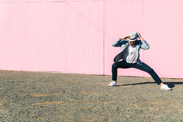 Young man in front of pink construction barrier, crouching, holding his hat