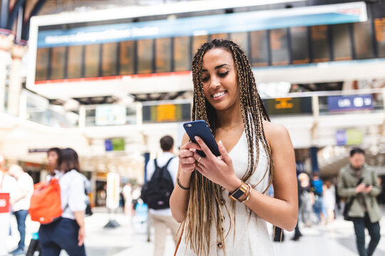 Portrait of happy young woman at train station using smartphone, London, UK