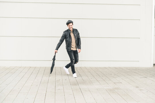 Young man walking around closed umbrella