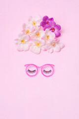Creative makeup concept with  pink glasses, eyelashes and orchid flowers on the pink background. Makeup concept.