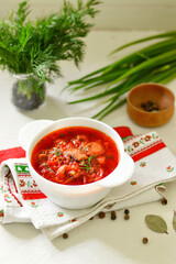 Ukrainian borscht in a white plate on a light background, decorated with fresh herbs