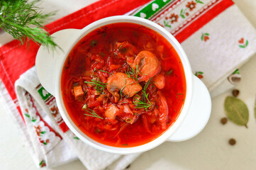 Ukrainian borscht in a white plate on a light background, decorated with fresh herbs