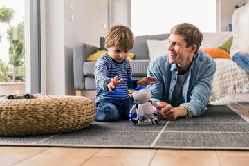 Father and son lying on floor, playing with toy robot