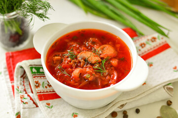Ukrainian borscht in a white plate on a light background, decorated with fresh herbs