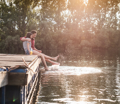 Happy young couple having a drink and splashing with water on jetty at a remote lake